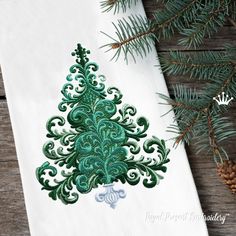 an embroidered christmas tree on a white napkin next to pine cones and evergreen needles,