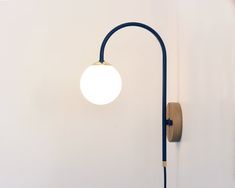 a wall light with a wooden arm and white ball on the top, against a white wall