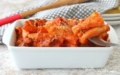 a white bowl filled with pasta and sauce next to a red handled fork on top of a table