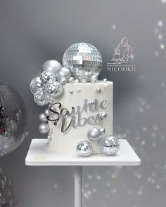 a white cake with silver decorations and disco balls around it on a stand in front of a mirror ball backdrop