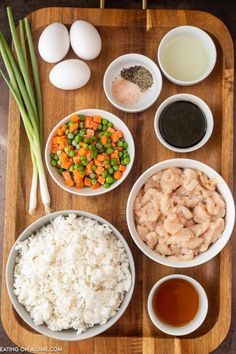 an assortment of food is displayed on a wooden tray, including rice, peas, carrots and eggs