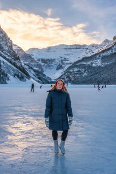 a woman standing on top of an ice covered field with mountains in the back ground