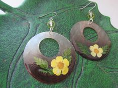 the earrings are decorated with yellow flowers and green leaves on top of a leafy surface