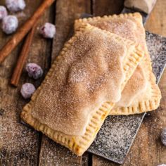 two pastries with powdered sugar sit on a plate next to cinnamon sticks and blueberries