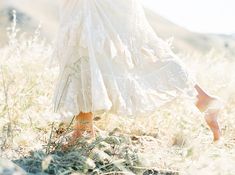 a woman in a white dress is walking through tall grass with her legs crossed and shoes on