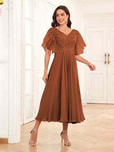 a woman standing in a room wearing a brown dress with ruffles on the shoulders