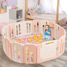 a baby sitting in a pink playpen with balls all over the floor and walls