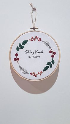 a cross stitch ornament hanging from a wooden hoop on a white background with the words baby hands written in red and green leaves