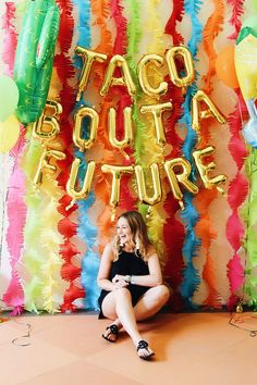 a woman sitting on the floor in front of a backdrop with taco bouta future balloons