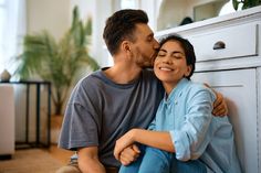 a man and woman sitting next to each other in front of a white dresser kissing