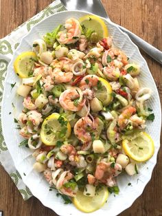 a white bowl filled with shrimp and lemons on top of a wooden table next to a fork