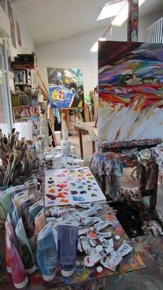 an artist's studio with lots of art supplies on the table and paintings in the background