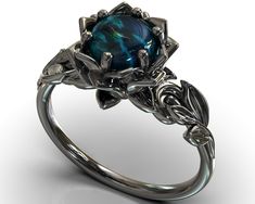 "Looking for a unique engagement ring to begin your life with your special love? Look no further than this amazing Australian Black Opal Black Gold Lotus ring. With its unique shape and sparkling Natural Black opal, it makes a one of a kind statement of your love and commitment. The band is created of solid, 14kt black gold, carved at the top into an elaborate design of leaves. The design draws the eye toward a center of black gold petals. The highlight of this piece is the rare black opal (Aust Elegant Black Flower Promise Ring, Elegant Black Flower Ring For Wedding, Black Flower Ring For Wedding, Black Opal Wedding Ring, Black Opal Engagement Ring, Engagement Ring Leaf, Black Opal Jewelry, Gothic Engagement Ring, Lotus Ring