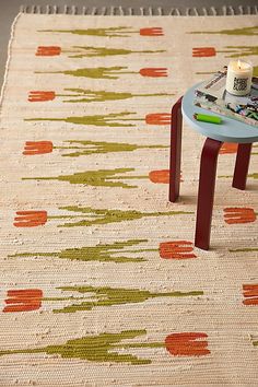 a small table with a candle on top of it next to a rug that has orange and green designs