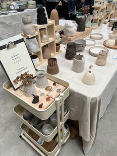 many different vases and bowls are on display at the table with a sign that says pottery