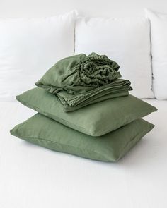 three pillows stacked on top of each other in front of a white bed with green sheets