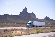 a semi truck driving down the road with mountains in the backgrouds behind it