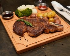 a wooden cutting board topped with steak, potatoes and broccoli next to utensils