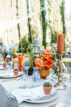 the table is set with blue and white dishes, orange candles, and flower arrangements