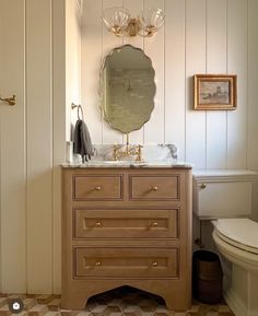 a white toilet sitting next to a bathroom sink under a mirror on top of a wooden dresser