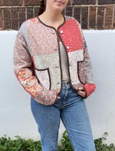 a woman standing in front of a white wall wearing jeans and a red cardigan