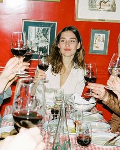 three women sitting at a table with wine glasses in their hands and one woman standing up to the camera