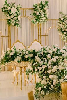 white flowers and greenery are arranged on gold chairs