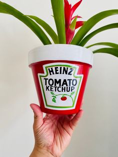 a hand holding up a cup with ketchup on it next to a plant