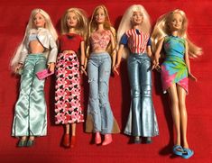 five barbie dolls are lined up on a red surface, one is wearing jeans and the other has a striped shirt