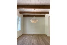 an empty living room with wood floors and white walls, including a chandelier hanging from the ceiling