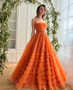 Introducing our elegant ensemble, radiating the soft allure of a Sunrise Orange hue, designed to captivate and charm at every soirée. The illusion plunging V-neckline tastefully teases, leading down to a meticulously handcrafted, fluffy tulle layered ruffle texture that whimsically dances with every step you take. The dress cinches gracefully at the waist, showcasing a decorative ribbon bow belt before unfolding into a classic A-line silhouette that celebrates your form. The floor-sweeping skirt Textured Wedding Gown, Orange Elegant Dresses, Bright Orange Formal Dress, Orange Ball Gown, Formal Orange Ruffled Dresses, Orange Dresses Formal, Orange Wedding Dress, Yellow Ruffled Party Gown, Yellow Ruffled Tulle Dress