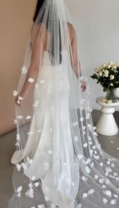 a woman in a wedding dress with white flowers on her veil, looking down at the floor