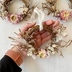 a person holding a wreath with dried flowers on it and two other wreaths behind them