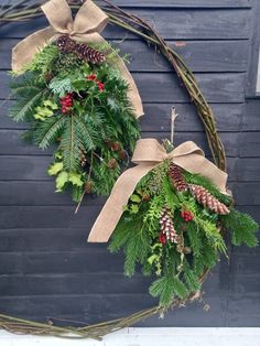 two wreaths with evergreen, pine cones and red berries hanging from the front door