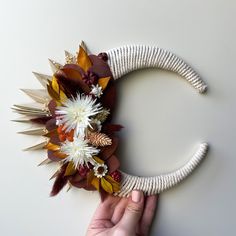 a hand holding a fake flower wreath on top of a white surface with other flowers