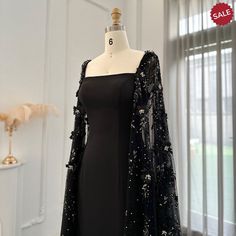 Elevate your evening look with the Dreamy Vow Luxury 3D Flowers Black Satin Arabic Evening Dress. The elegant mermaid silhouette is adorned with delicate 3D flowers and a stunning cape, adding a touch of sophistication. Made with high-quality satin, this dress is perfect for formal parties and special occasions. Experience elegance and luxury in our Dreamy Vow Arabic Evening Dress. Adorned with intricate 3D flowers, this black satin dress is perfect for formal parties. The accompanying cape adds Black Masquerade Dress With Sleeves, Luxury Elegant Dress With Cape Sleeves, Luxury Black Dresses With Cape Sleeves, Luxury Elegant Evening Dress With Cape Sleeves, Luxury Satin Evening Dress For Formal Occasions, Luxury Black Gown For Party, Black Mermaid Dress With Cape, Black Caped Dress, Luxury Black Dress With Cape Sleeves