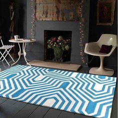 a living room with a rug, chair and table in front of a fire place