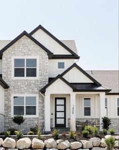 a white brick house with black trim and windows on the front door is surrounded by large rocks