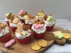 some cupcakes are sitting on a wooden board with candy and coins around them