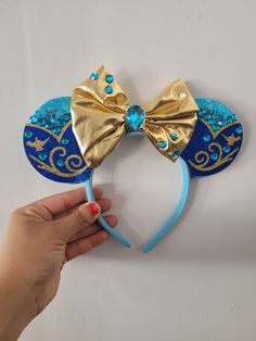 a hand holding up a blue and gold mickey mouse ears headband with sequins