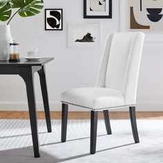 a white chair sitting in front of a table with pictures on the wall behind it