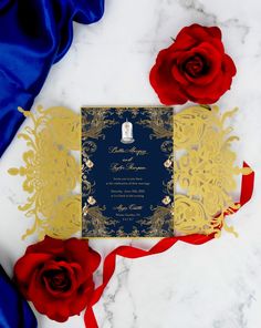 a wedding card with red roses and blue satin on the table, next to it