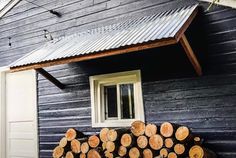 logs stacked on top of each other in front of a black house with a metal roof