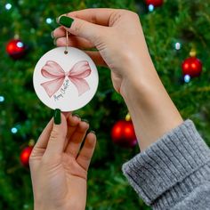 a person holding up a christmas ornament with a pink bow on it's side