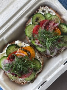 two slices of bread with vegetables on them in a plastic container next to a blue napkin