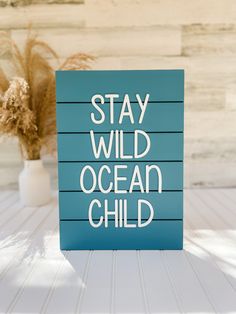 a blue sign that says stay wild ocean child on top of a white table next to a plant