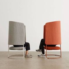 two people sitting on chairs facing each other in front of a white wall and floor