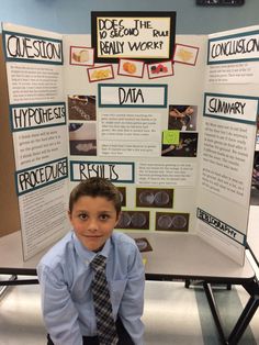 a young boy sitting in front of a poster with information about his work on it