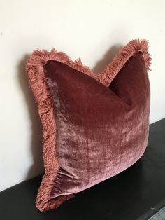 a pink velvet pillow sitting on top of a black shelf next to a white wall