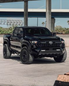 a black toyota truck parked in front of a building under an overpass with palm trees